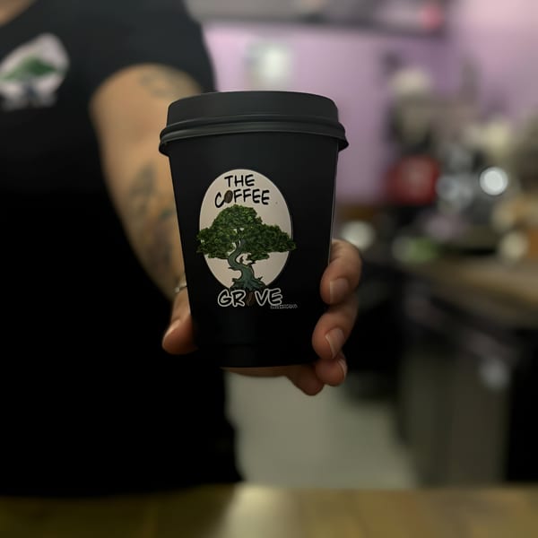 A hand extends a black Coffee Grove Corp cup with a green tree logo towards the viewer.