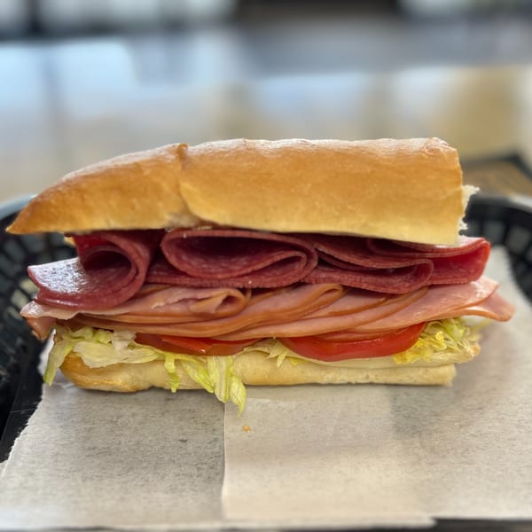 A large deli sub sandwich with various meats, lettuce, and tomatoes on a white paper.
