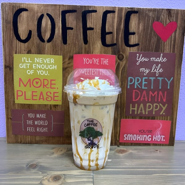 Iced coffee with whipped cream and caramel drizzle in front of a wooden sign with coffee-themed quotes.
