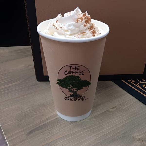 A Coffee Grove Corp coffee cup with whipped cream and cinnamon on a wooden table.